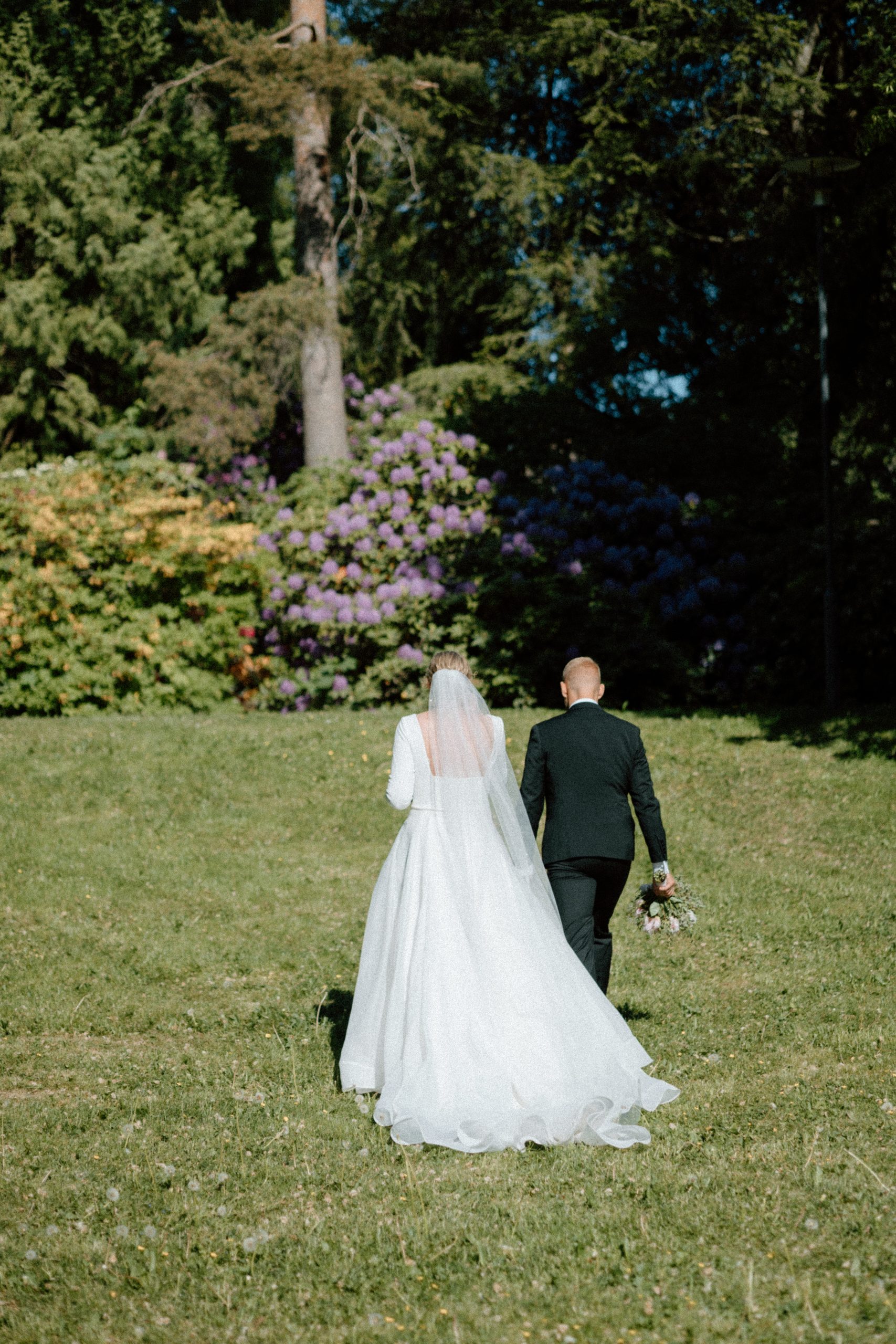 Bride and groom in a park walking away from camera